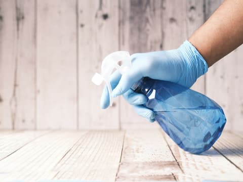 Hand im Handschuh mit Sprühflasche beim Wischen